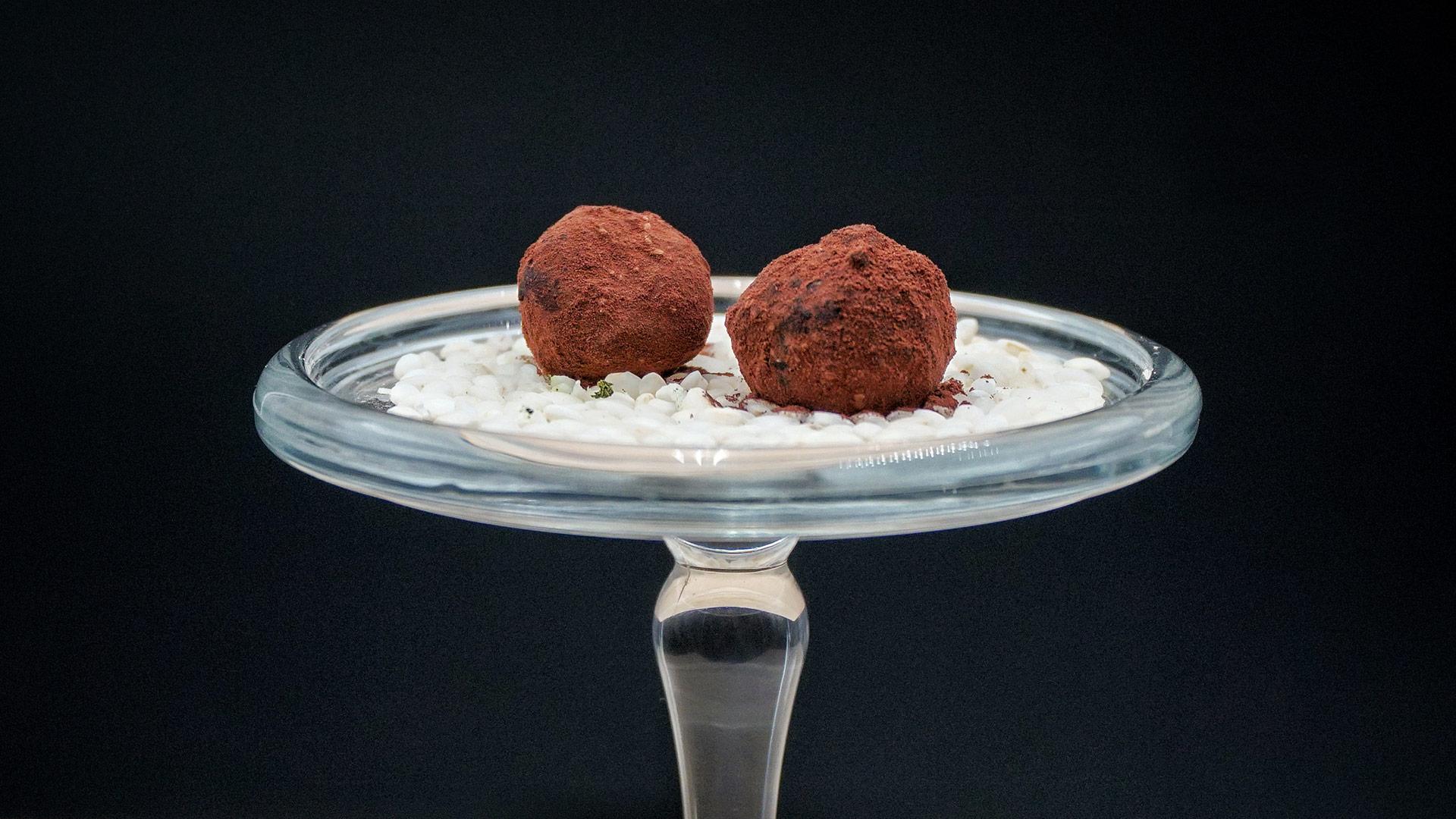 Due tartufi al cioccolato su un piatto di vetro con sfondo nero.