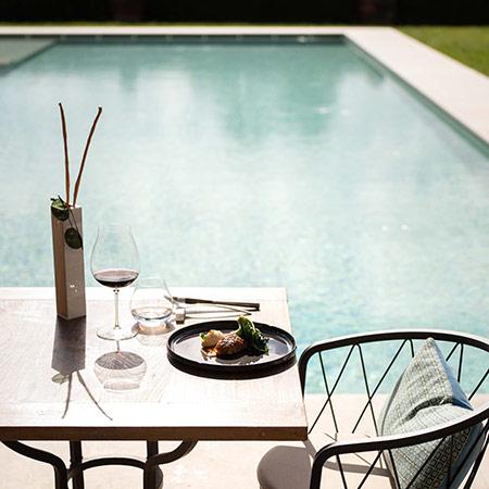 Tavolo elegante con vino e cibo, accanto a una piscina luminosa.