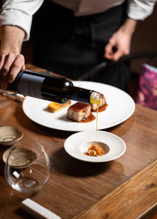 Un cameriere versa olio su un piatto con antipasto raffinato in un ristorante elegante.