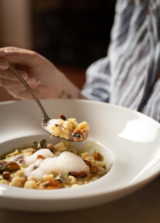 Piatto di pasta con cozze, schiuma e ceci in un piatto bianco elegante.