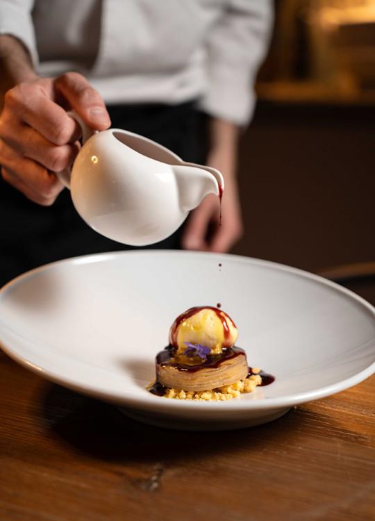 Dessert raffinato con salsa versata sopra, servito su un piatto bianco elegante.