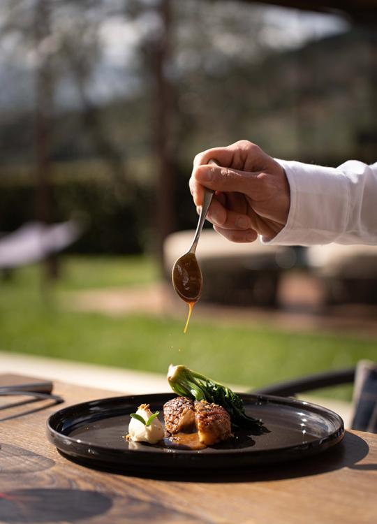 Piatto gourmet con salsa versata su carne e verdure su un piatto nero.